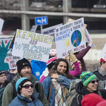 People at protest holding signs including one that says Refugees are Welcome Here and Immigrants Make America Great
