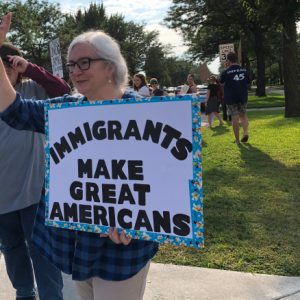woman standing outside while holding a sign that says "Immigrants make great Americans"