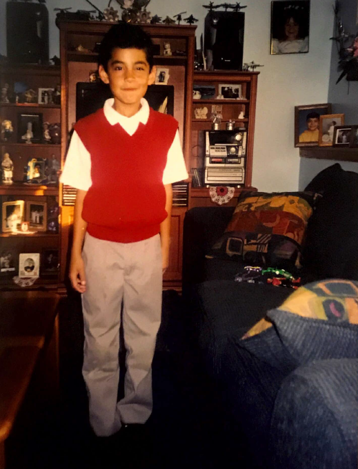 José in school uniform. Red vest, white polo t-shirt, tan pants