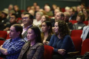 people sitting in a theater listening to panel of speakers