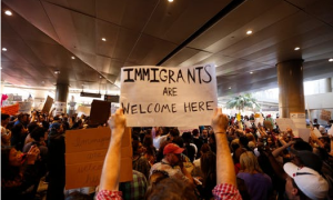 person holding sign that says "immigrants are welcome here" at a rally