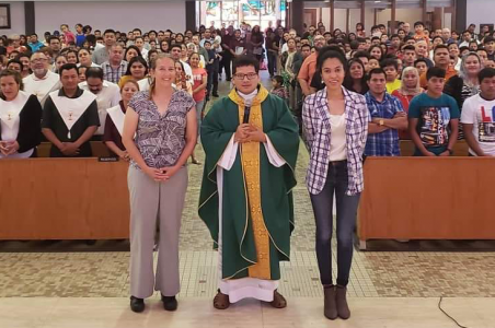 Kathy and Joyce at St. Mary's church in Worthington standing with a Father in front of the congregants sitting in pews